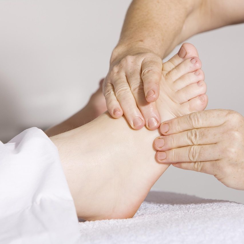 • Fuss-Reflexzonen revital Massage Eine Person erhält eine Fußmassage mit zwei Händen, die den Knöchel und den Fuß berühren.