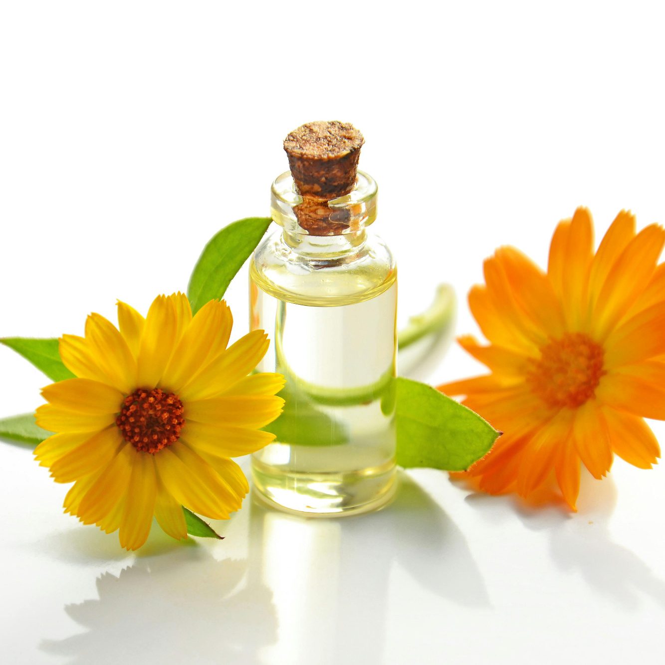 • Aroma Massage mit ätherischen Ölen Glasflasche mit Öl, umgeben von orangefarbenen Ringelblumen und grünen Blättern.