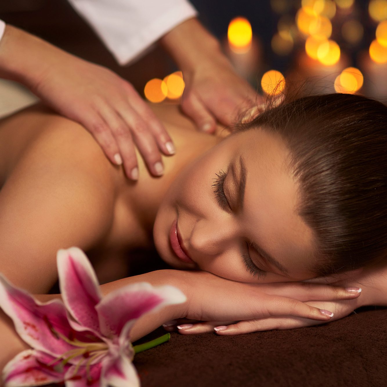 • Kopf-Schulter-Rücken Thai Massage Frau erhält entspannende Massage mit Lilie im Vordergrund und weichem Licht.