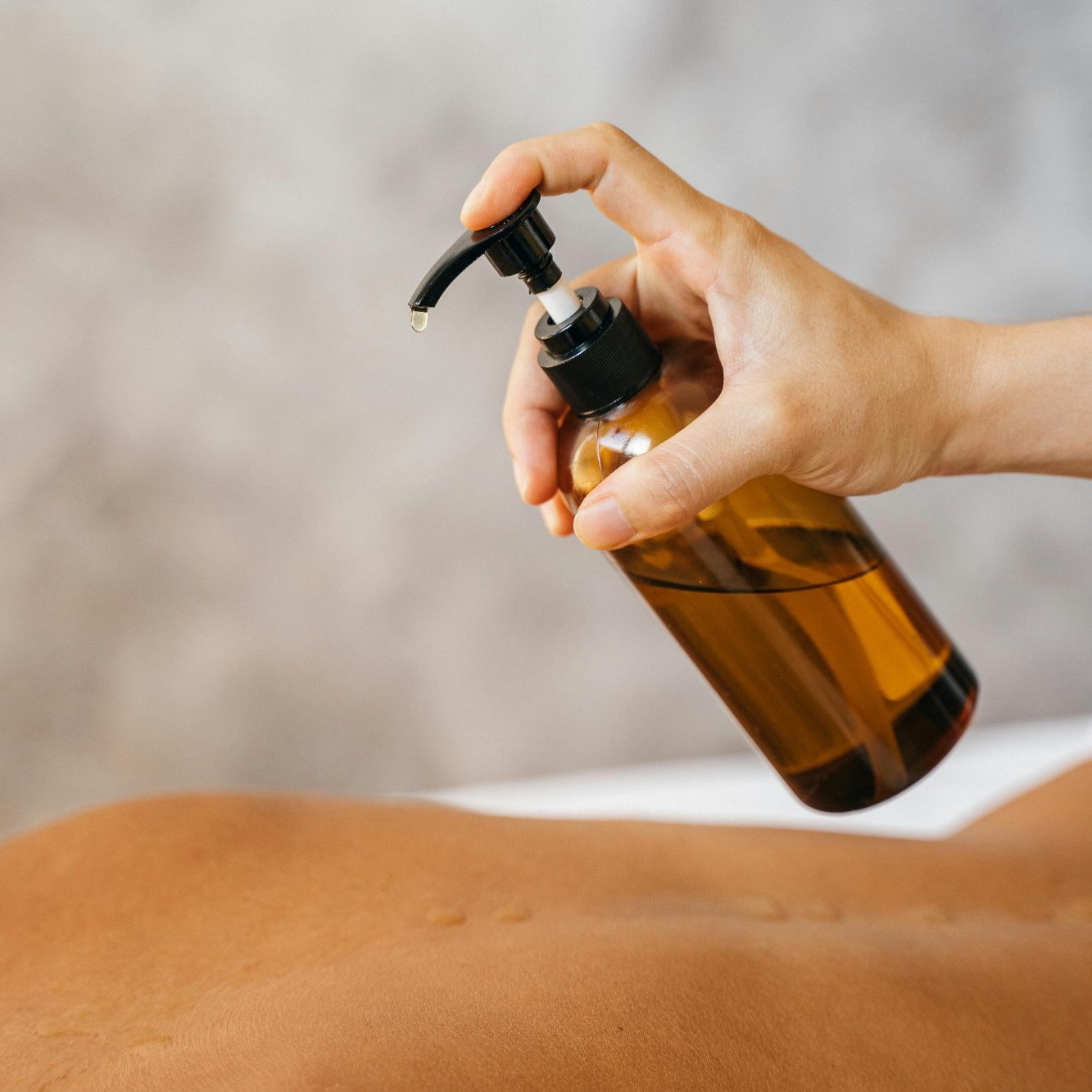 Öl-massage Händedruck auf eine Flasche mit Öl über einem nackten Rücken.